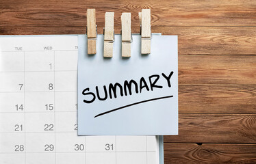 Blue sticker attached to a calendar on a wooden background with text Summary
