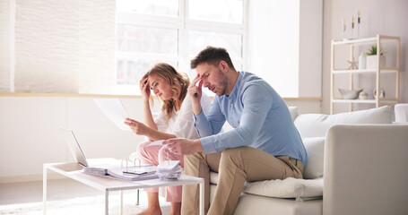 Shocked Young Couple Sitting On Sofa Looking At Bill