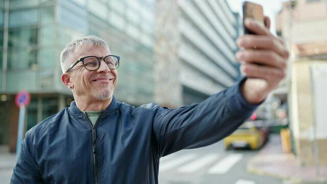 Middle age grey-haired man smiling confident making selfie by the smartphone at street