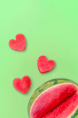 Fototapeta na wymiar Cut watermelon and watermelon hearts on a green background