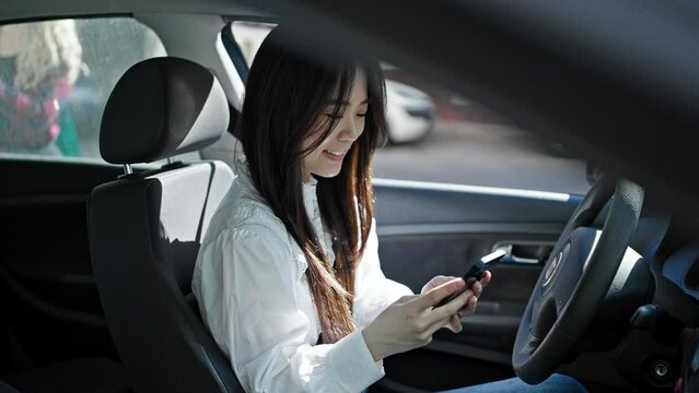 Young chinese woman using smartphone sitting on car at street