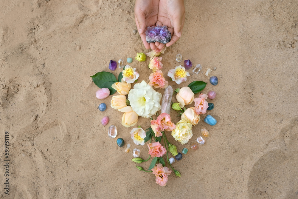 Wall mural hands with gemstones and flowers for crystal ritual on sand natural background. esoteric spiritual w