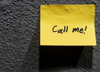 A yellow note on dark wall with text written CALL ME . Concept of telling someone to make a phonecall.
