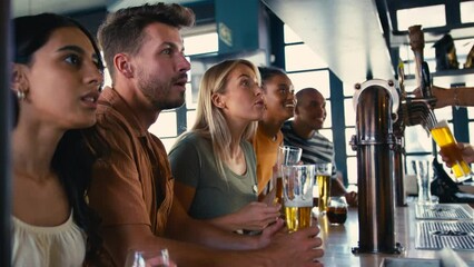 Multi-cultural group of friends in sports bar celebrating as they watch game on TV together - shot in slow motion