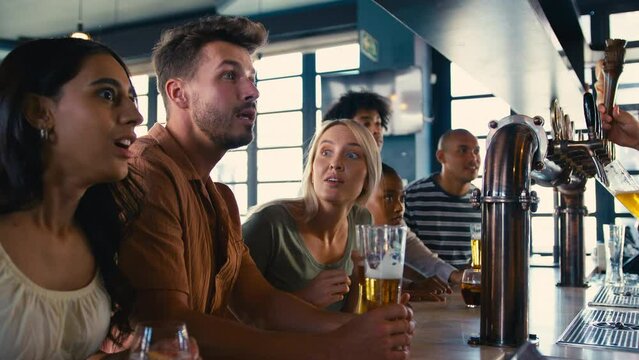 Multi-cultural group of friends in sports bar celebrating and giving each other high fives as they watch game on TV together - shot in slow motion