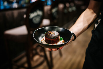waiter hand hold Basque cheesecake with Chocolate and cream in bowl
