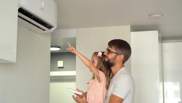 Father with little girl check cold air of conditioner, turn on using remote control. Happy family adjust comfortable temperature