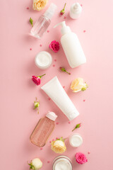 Unleash your natural beauty with this tender skincare concept. Top view flat lay of beautiful pump bottle, pipette, elegant cream bottles and tubes with rose flowers on pastel pink background