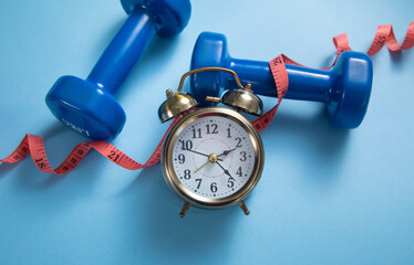 Measuring tape, alarm clock and dumbbells on the blue background.
