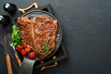 Steaks T-bone. Sliced beef grilled T-bone or porterhouse meat steak with spices rosemary and pepper on black marble board on old wooden background. Top view. Mock up.