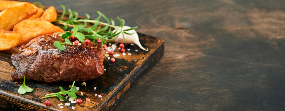 Steaks. Sliced grilled meat steak New York, Ribeye or Chuck roll with with garnished with salad and french fries on black marble board on old wooden background. Mock up.