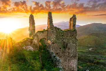 Fototapeta premium immersive landscape of old castle ruins on foreground and beautiful mountains with sunset with clouds on background