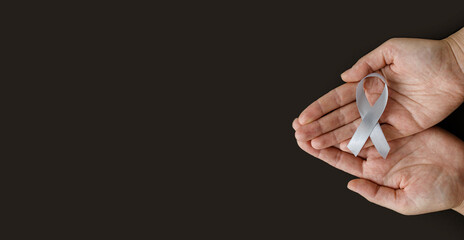 World Brain Tumor day. Person's hands are holding a gray ribbon on a black background. This is observed every year on June 8th.