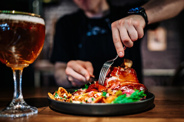 man cuts a pork knuckle with a knife and fork