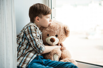 Sadness outside the window. One child boy abandoned in an old abandoned house with a teddy bear. He...