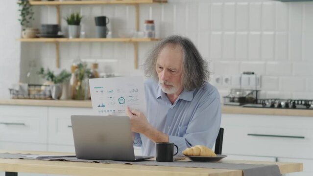 an elderly middle-aged man works at home remotely showing a paper with sales statistics graphics. The concept of remote work from home by video conference