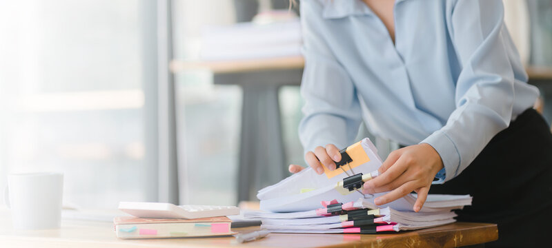 Cropped shot of businesswoman is sifting through stacks of paper files and folders that contain both incomplete and completed documents. Selective focus