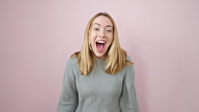 Young blonde woman standing with surprise expression over isolated pink background
