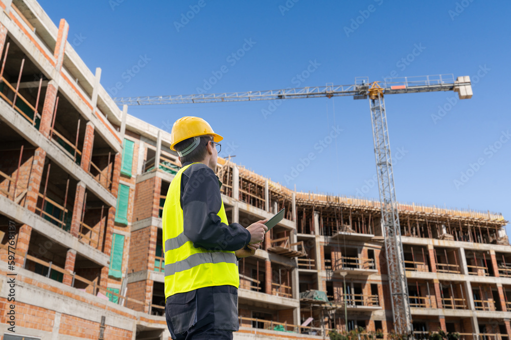Poster Engineer with a digital tablet on the background of a building under construction	