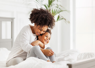 Happy ethnic family. African american mother and daughter play and laugh in bed.