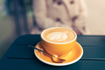 Cup of cappuccino with latte art. Coffee in yellow cup on table in cafe. Enjoy moment, take a break.