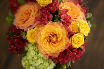 Floral arrangement of gorgeous orange, yellow, and red flowers on a brown table with space for text.