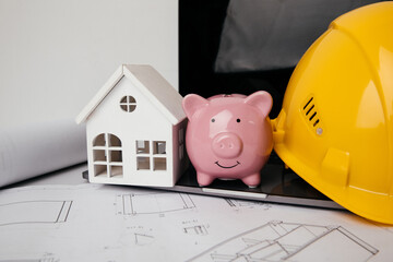 Yellow helmet, piggy bank and model of house in engineer office