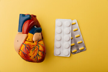 Human heart model with pills on a yellow background, close-up