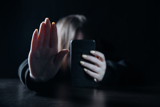 Teenager female girl with smartphone in her hand felling lonely and hopeless sitting in a dark room. Cyber bullying and harassment concept