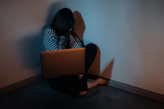 Young teenager female girl sitting with a laptop in a dark room, concept of cyber bullying