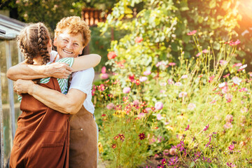 Rear view of young teenager girl with cute hairstyle two braids hugging her happy loving grandmother at summer countryhouse outdoor.