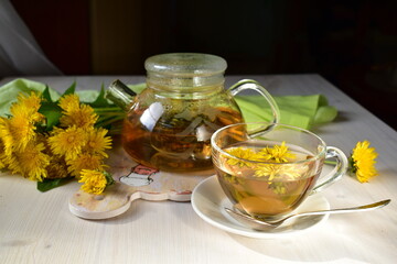 green tea with dandelions in a teapot and glass cup on a wooden table