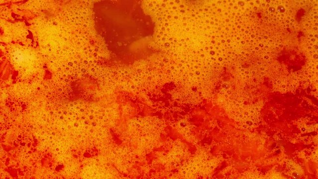 Red liquid food boils. Ukrainian national food. Ukrainian borscht. Ethnic beetroot soup. Beautiful orange bulbs in boiling food in a saucepan. Boiling vegetables beetroot, potatoes, tomatoes, cabbage