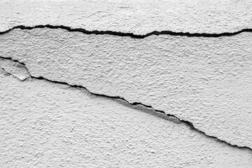 Two big diagonals cracks on old plastered wall. Close-up. Copy space. Black and white photo. Selective focus.