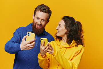 Man and woman couple smiling merrily with phone in hand social media viewing photos and videos, on yellow background, symbols signs and hand gestures, family freelancers.