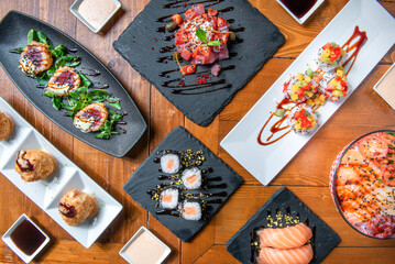Symmetrical composition of Japanese food from above on wooden table, sushi, sashimi, tempura, salmon poke , fish bawls, tuna tartare and vegetables. 