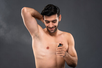 Shirtless handsome Caucasian man using deodorant body spray in light gray isolated background...