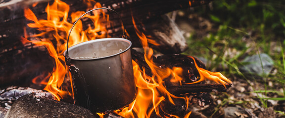 Kettle stands on fire. Cooking food at fire in wild. Beautiful big log burns in bonfire close-up....