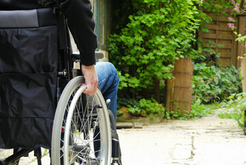 A disabled person in a wheelchair. A man with reduced mobility in an alley with vegetation.