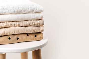 Stack of baby clothes. Cotton clothes and muslin swaddle blanket in white and beige colors. Clean freshly laundered, neatly folded kids clothes on table. - obrazy, fototapety, plakaty