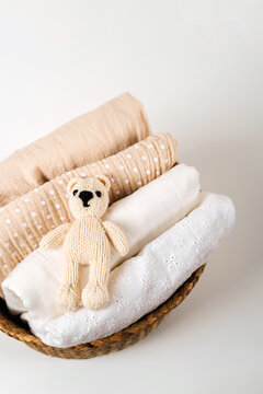Stack of baby clothes with cute little teddy bear in the basket. Cotton clothes and muslin swaddle blanket in pastel colors. Clean freshly laundered, neatly folded kids clothes.