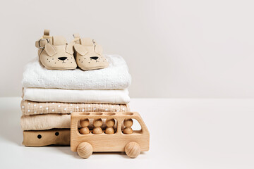 Stack of baby clothes with  baby shoes and wooden toy car. Cotton clothes and muslin swaddle blanket in pastel colors. Clean freshly laundered, neatly folded kids clothes. - obrazy, fototapety, plakaty