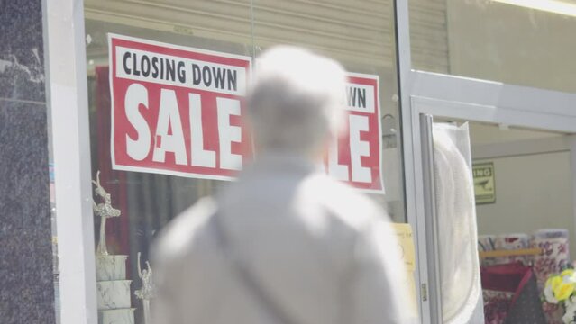 Closing down sale sign on a high street shop as pedestrians walk past, in slow motion
