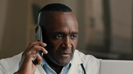 African American doctor adult man work with computer at hospital use modern medical technology call patient remote by mobile phone male professional therapist consulting distant telemedicine concept