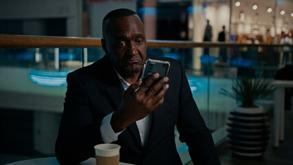 50s Ethnic African American man entrepreneur middle-aged businessman talk video call with mobile phone conference answer no dissatisfied talking with cellphone with business colleague sitting in cafe