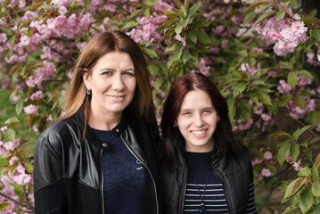 Fototapeta premium Happy and beautiful mother and daughter are resting together in spring and talking about life against background of a blooming garden, they have recovered their communication after long break