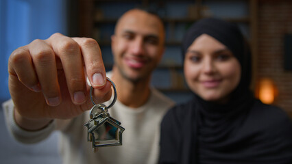 Happy homeowners african american arabian muslim multiracial diversity couple showing keys from new home real estate house looking at camera relocation day bank loan mortgage for young family concept