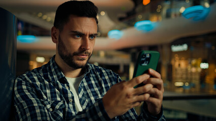 Concentrated pensive caucasian hispanic businessman thinking worker serious man looking at mobile phone screen texting message typing on smartphone chatting online app buying goods in shopping center