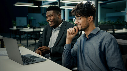 Two businessmen business partners office African American man client talk with Indian businessman colleague diverse ethnic multiracial men laughing having fun discuss online project on computer laptop