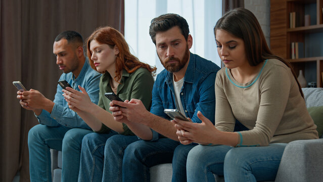 Sad man look at friends mobile phone addicted multiracial people lost in gadgets overuse social media networks chatting online diverse boring women men sit in row at home ignoring smartphone addiction